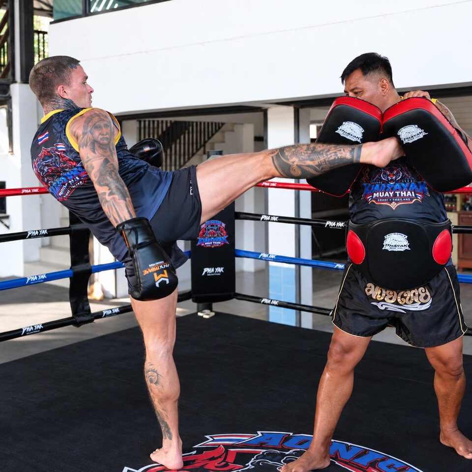 A student lands a high kick on the pads held by a Kiat Phayak trainer in the ring