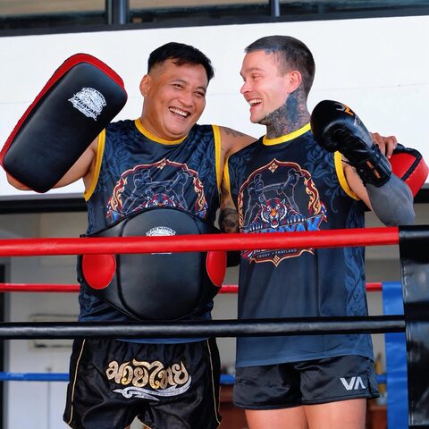 A trainer and a student laugh together at the ropes after a round